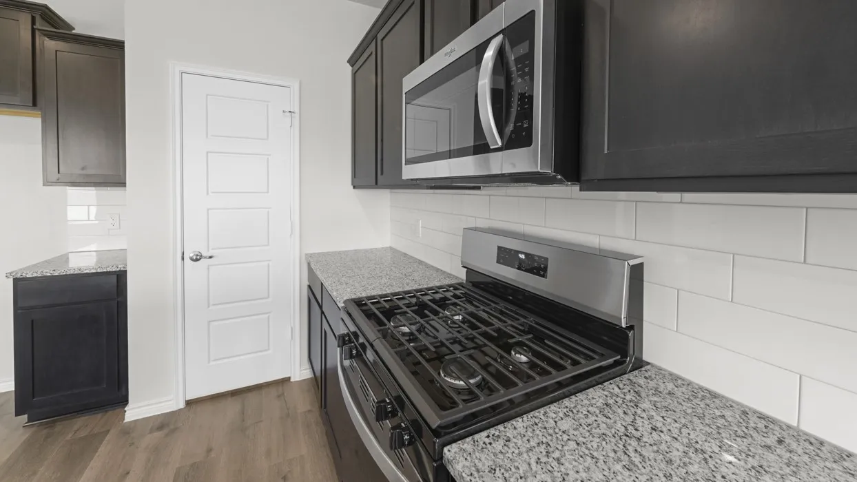Dark wood-finish cabinetry, stainless steel microwave, stainless steel gas range, stone-finish countertops, and white subway tile backsplash