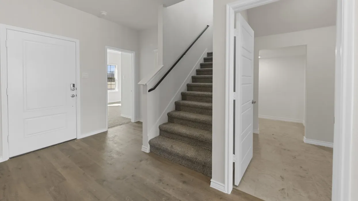 Wood-finish flooring, carpeted staircase with a black handrail, white interior doors, and neutral wall tones