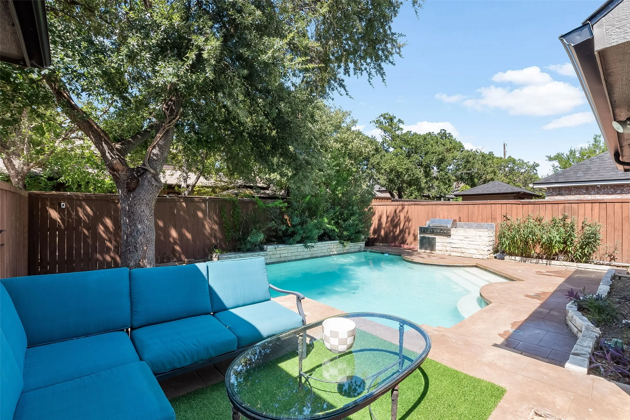 Private backyard featuring a swimming pool, integrated outdoor grill, stone retaining walls, and mature landscaping
