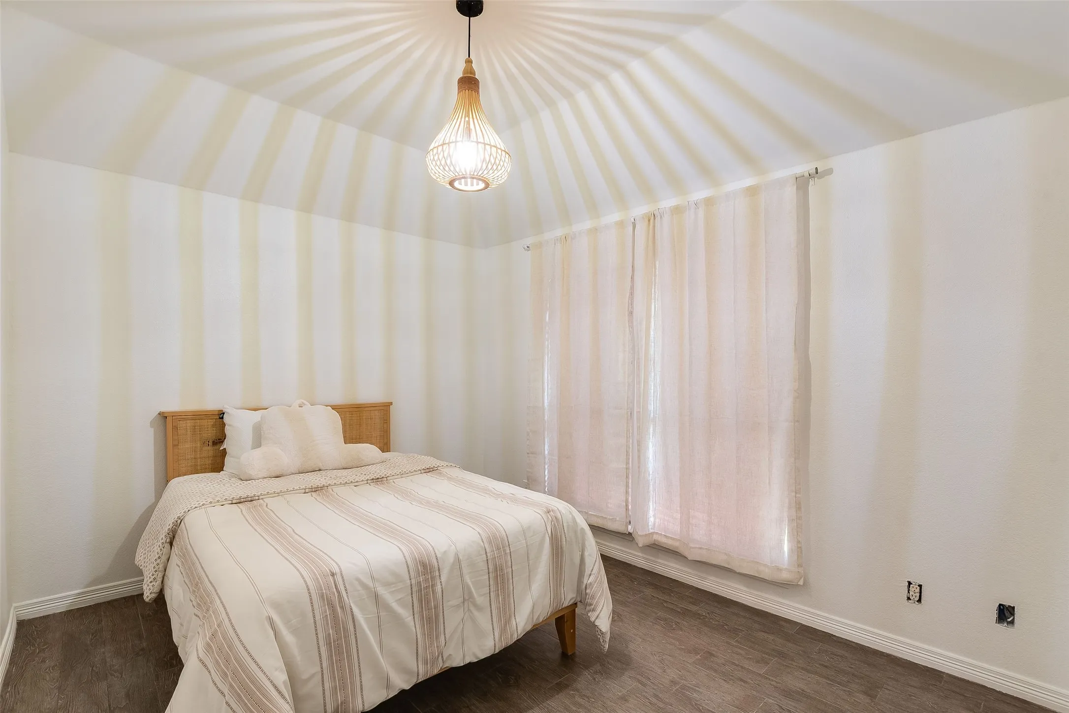 Vaulted ceiling featuring a decorative pendant light fixture, wood-finish flooring, and window with sheer curtains