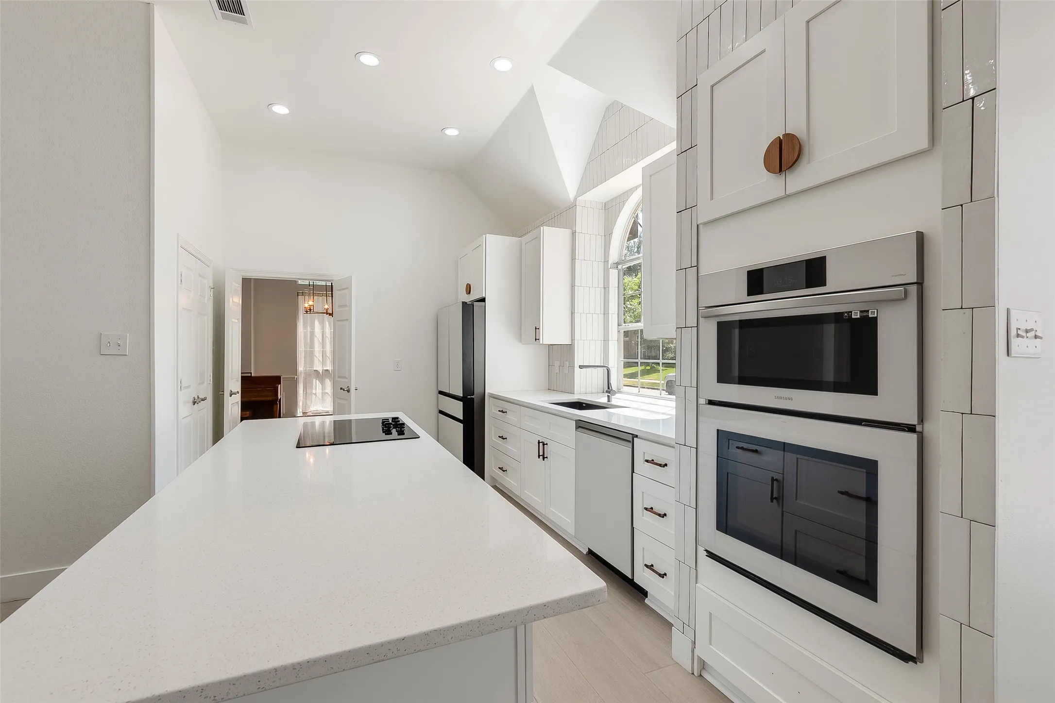 Contemporary kitchen featuring a vaulted ceiling, recessed lighting, white cabinetry, integrated stainless steel appliances, and a central island with a cooktop
