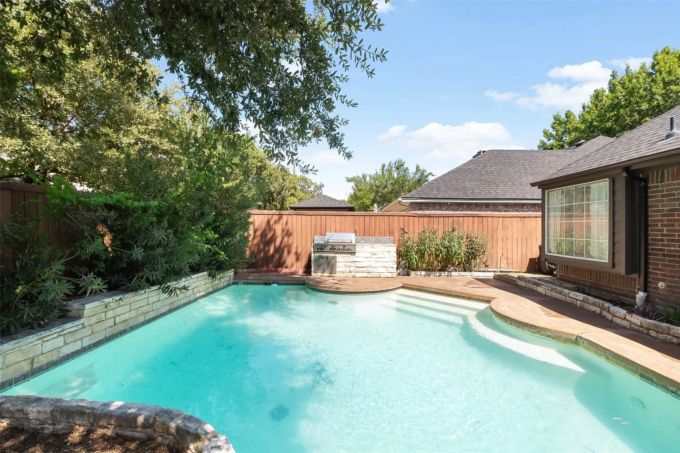 Resort-style backyard oasis featuring a sparkling saltwater pool with integrated spa jets, surrounded by mature landscaping and wooden privacy fencing