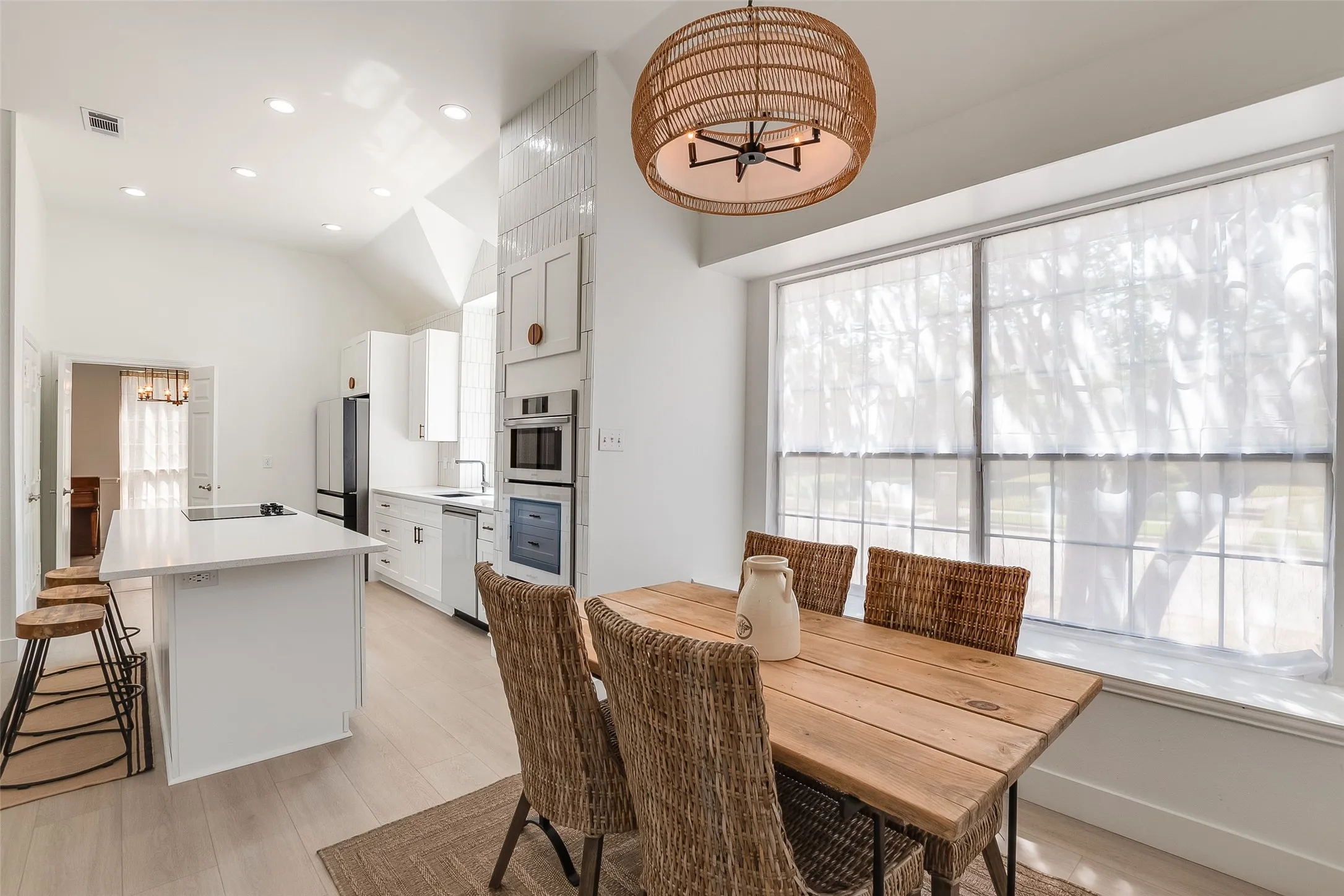 Vaulted ceiling with recessed lighting, integrated double ovens, kitchen island with built-in sink, light wood-finish flooring, and a window with a deep sill