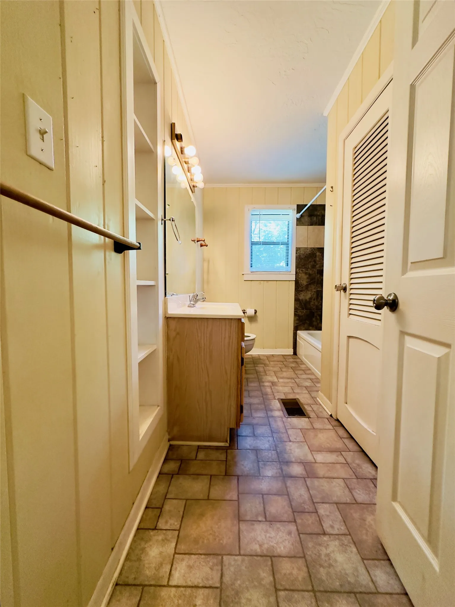 Bathroom featuring patterned tile flooring, a single vanity with wood-finish cabinetry, built-in shelving, and a window