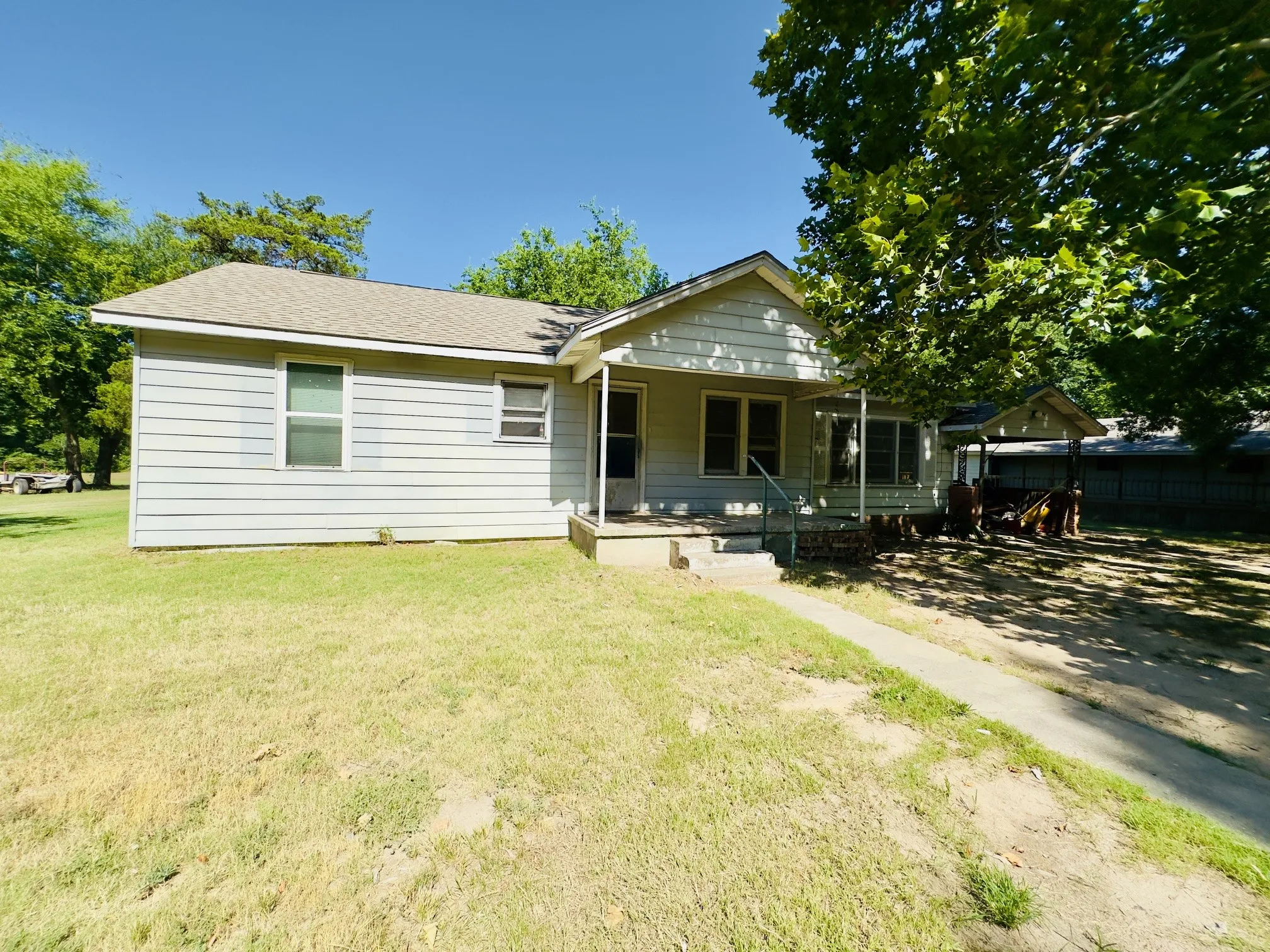 Light-colored siding exterior with a covered front porch, asphalt shingle roof, and a concrete walkway