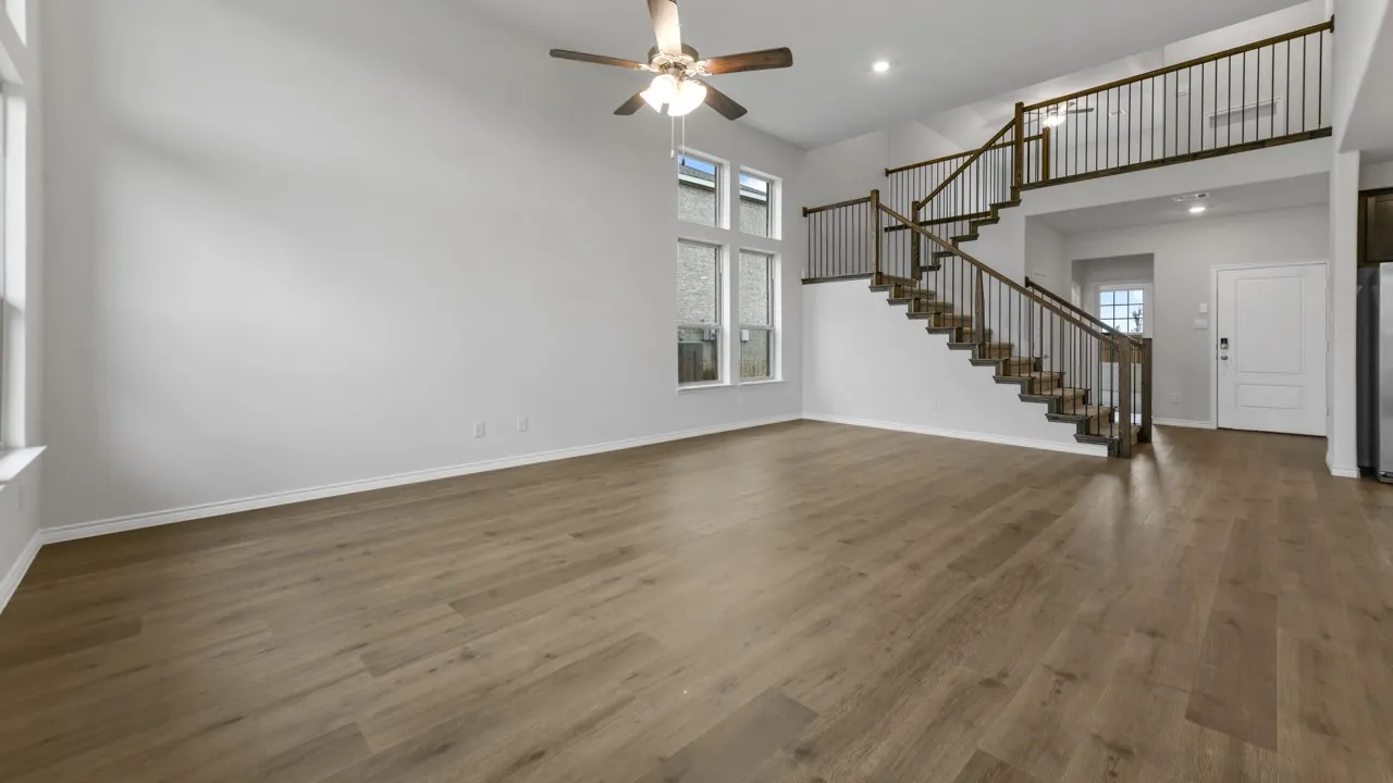Spacious living area featuring wood-finish flooring, high ceilings, multiple windows, and a ceiling fan