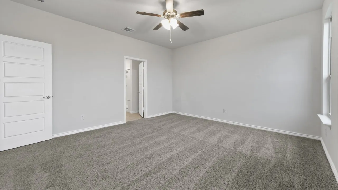 Spacious room featuring gray carpeting, light gray walls, a ceiling fan with light, and a white paneled door