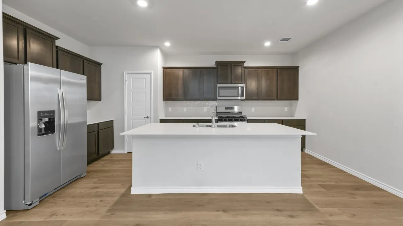 Kitchen featuring wood-finish flooring, dark wood cabinetry, white countertops, stainless steel appliances, and a central island with an undermount sink