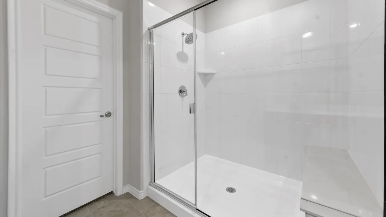Shower with clear glass enclosure, white subway tile surround, built-in shelving, chrome fixtures, and a white shower pan