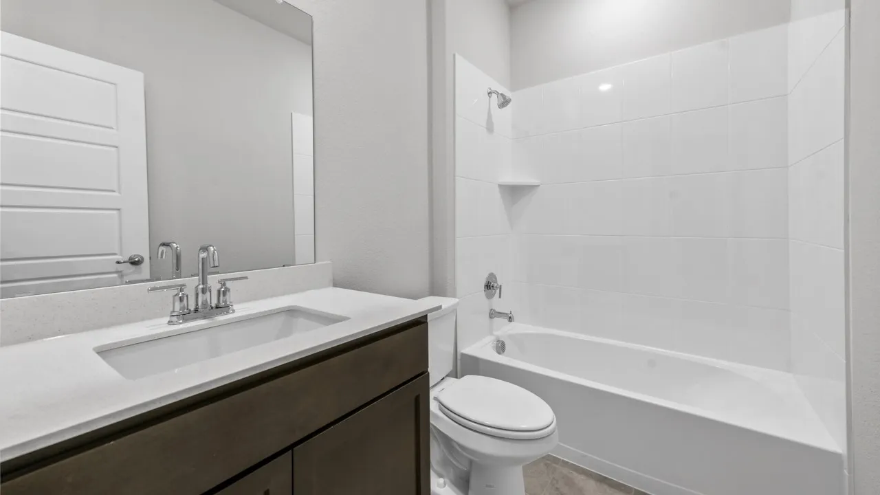 White tile tub surround, chrome fixtures, dark wood-finish vanity, integrated sink, and a framed mirror