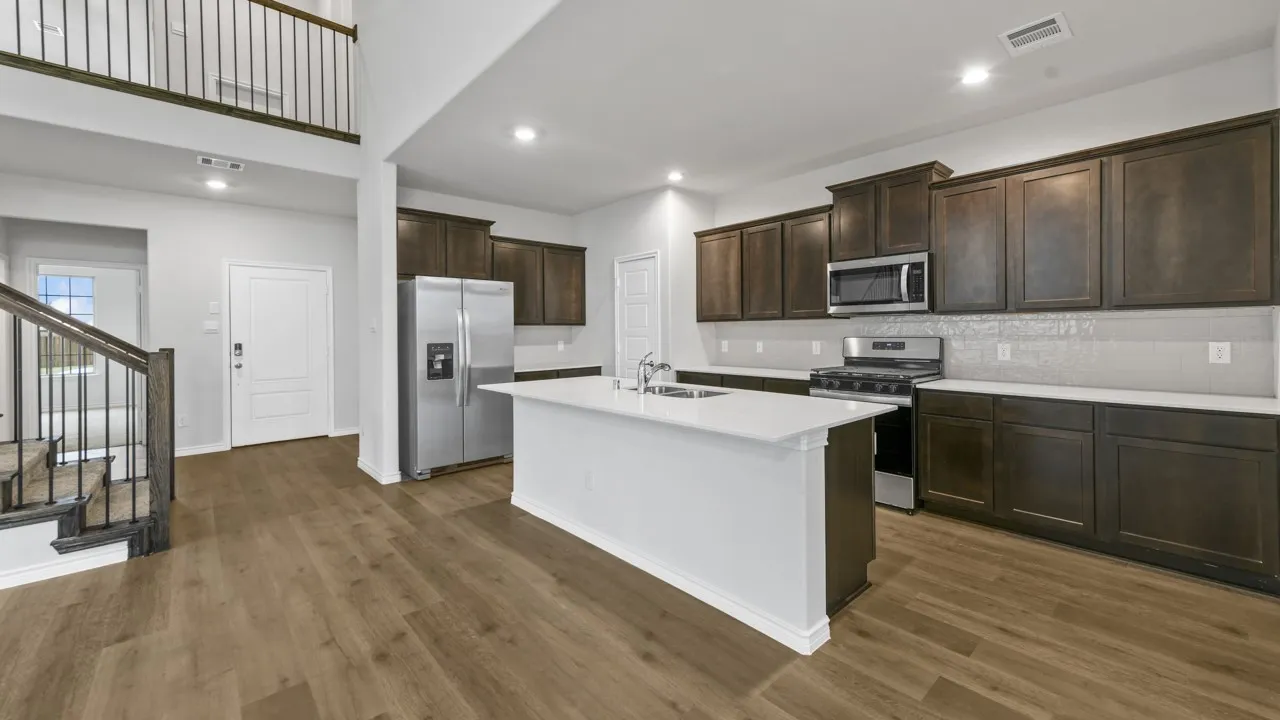 Modern kitchen featuring stainless steel appliances, white quartz countertops, a large waterfall-edge island, dark cabinetry, and wood-finish flooring throughout the open-concept living space