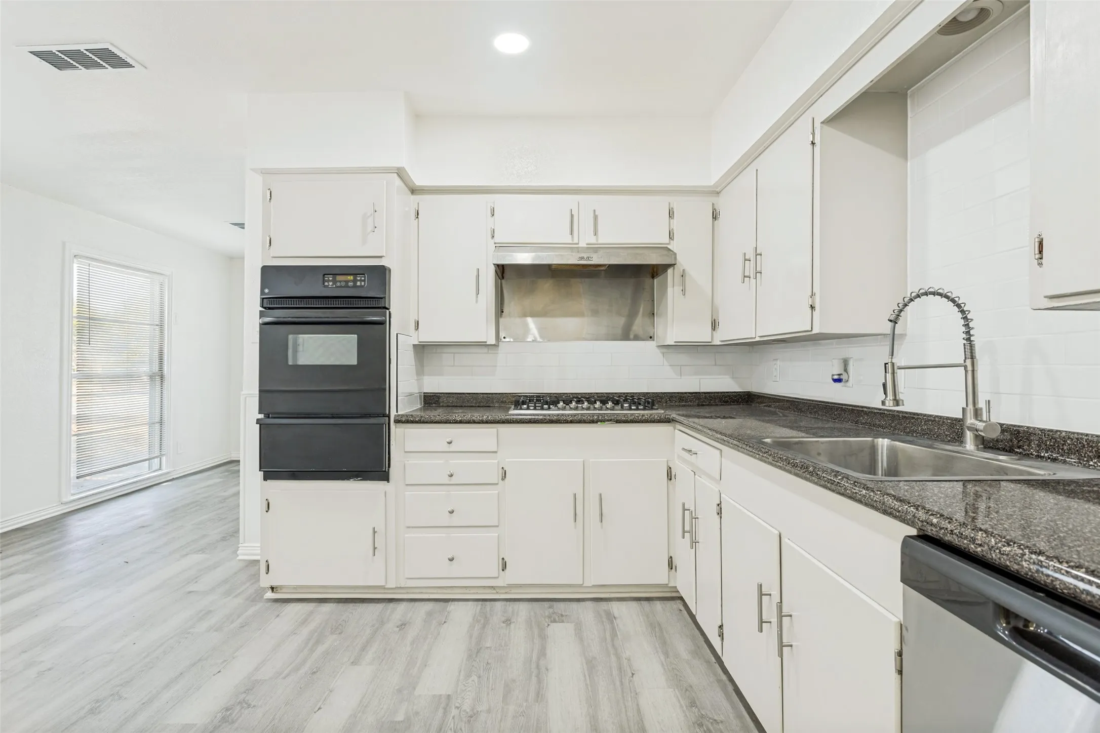 Kitchen featuring white cabinetry, dark speckled countertops, stainless steel sink with a gooseneck faucet, white subway tile backsplash, and wood-finish flooring