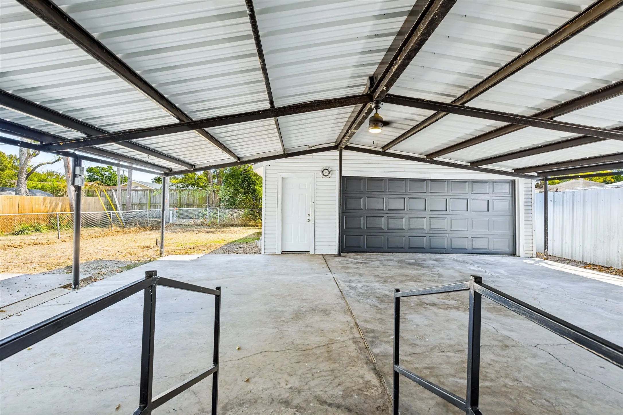Covered concrete carport featuring an attached garage with a dark panel door, and an exterior side door