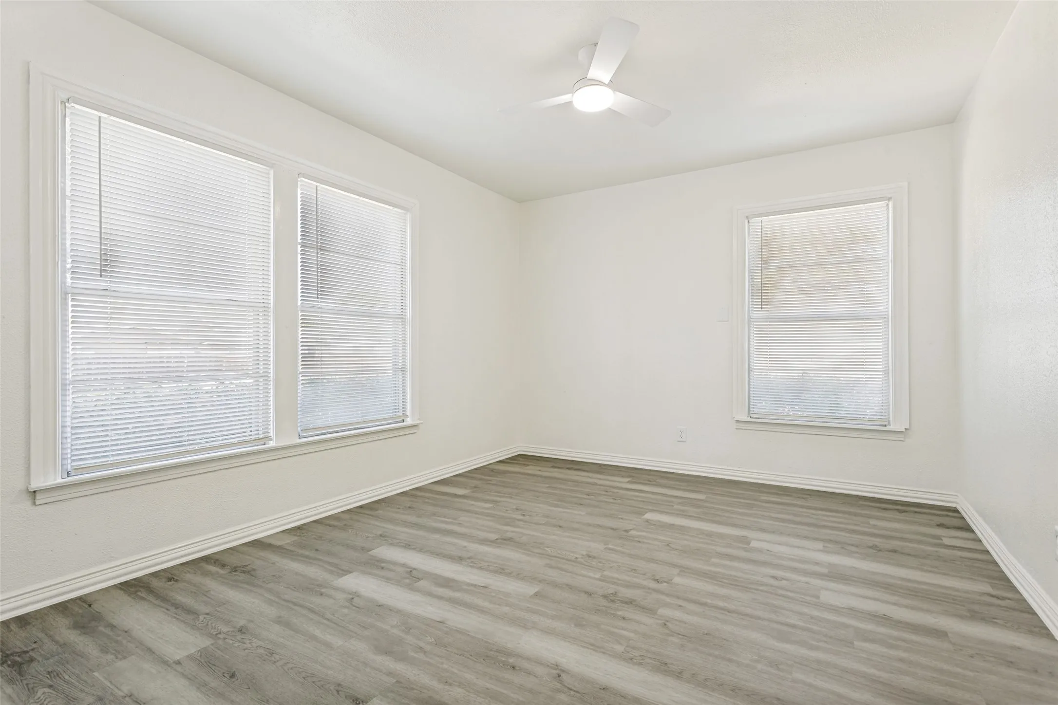 Light wood-finish flooring, white walls, multiple windows, and a ceiling fan