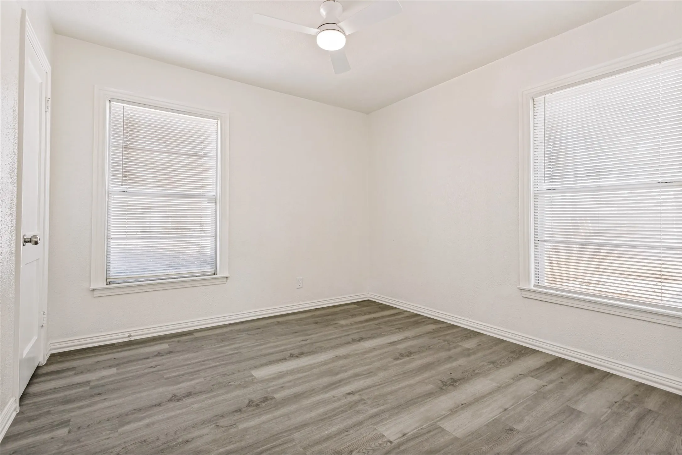 Light-toned wood-finish flooring, white walls, and built-in ceiling fan with integrated lighting
