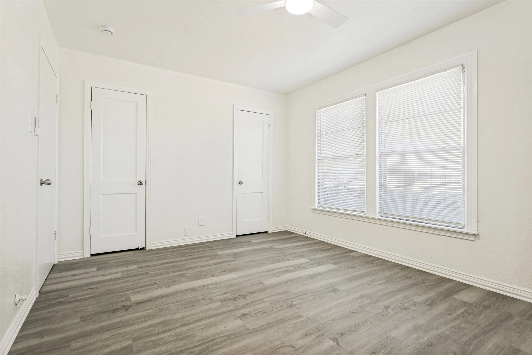Wood-finish flooring, white walls, two panel doors with chrome hardware, and a ceiling fan