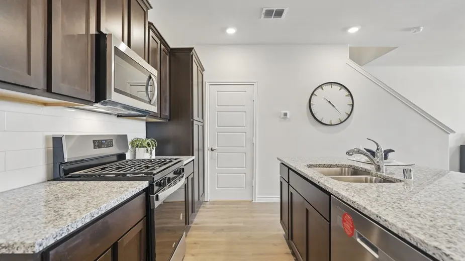 Kitchen featuring light-toned wood-finish flooring, dark wood cabinetry, stainless steel appliances, and light-toned speckled countertops