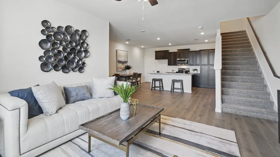 Open-concept living area with wood-finish flooring, a kitchen featuring dark wood cabinetry and a central island, and a carpeted staircase