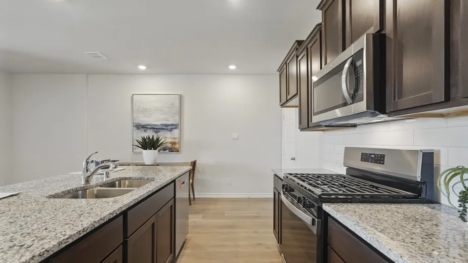 Kitchen featuring dark wood-finish cabinetry, light speckled countertops, stainless steel appliances, a double basin sink, and wood-finish flooring