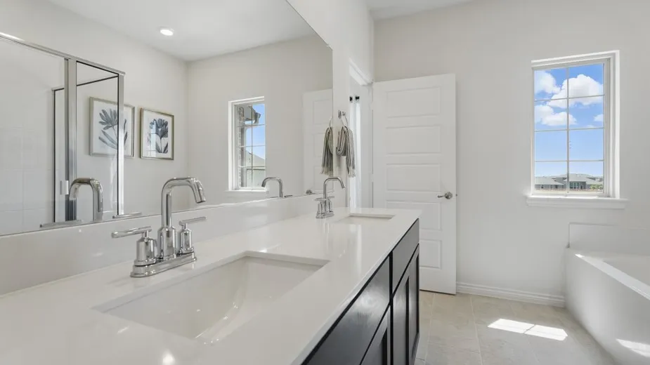 Dual vanity with chrome fixtures and white countertop, full-width mirror, built-in bathtub, and window with grid pattern