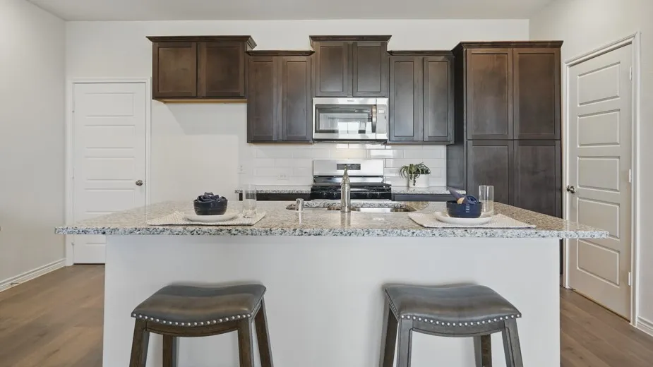 Kitchen island with a light-toned countertop, stainless steel sink, dark wood-finish cabinetry, built-in microwave, and subway tile backsplash