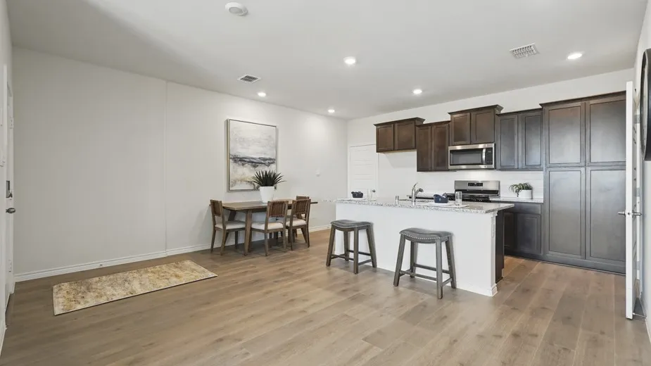 Wood-finish flooring, recessed lighting, white walls, kitchen island with seating, and dark wood-finish cabinetry
