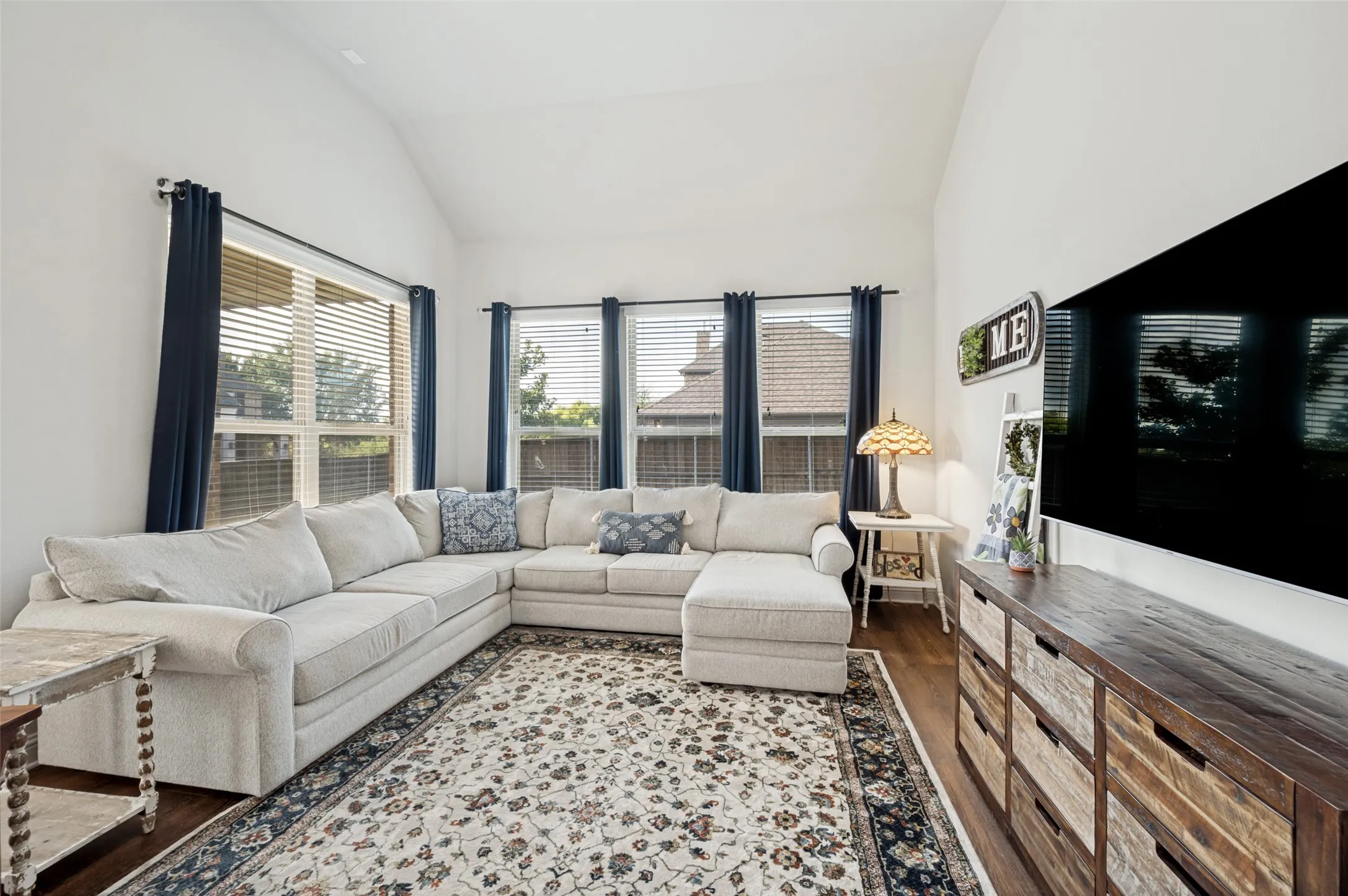 Bright and spacious living area featuring vaulted ceilings, beautiful wood flooring, and a wall of windows that fills the room with natural light.