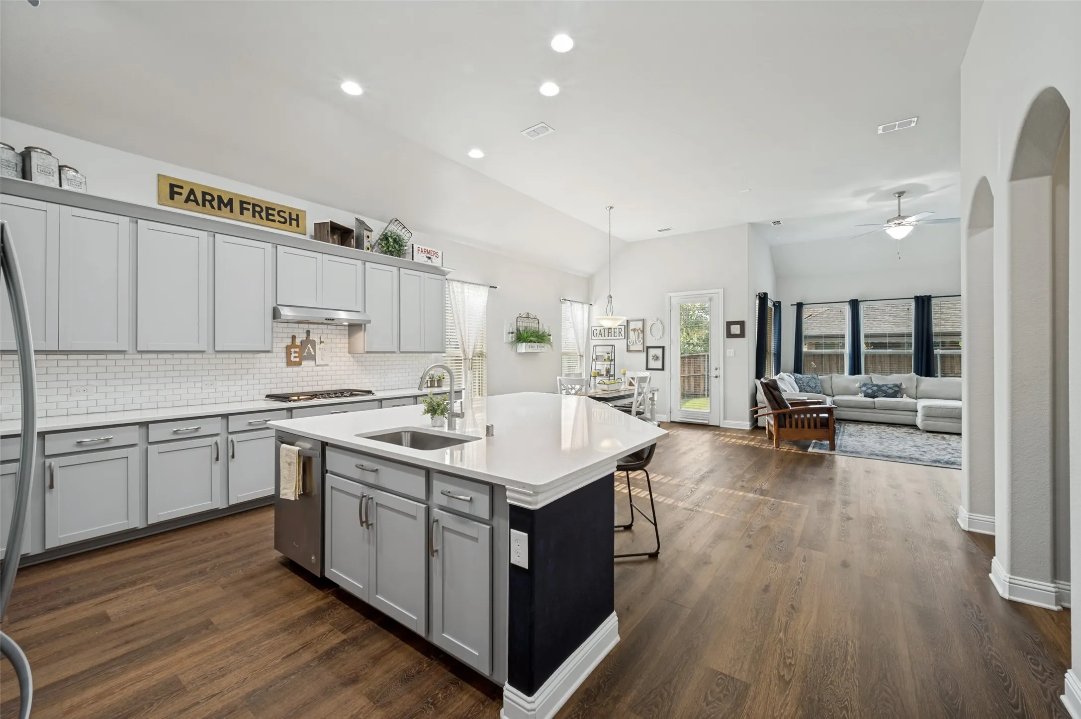 Spacious kitchen featuring a large center island with sink and seating, abundant cabinetry, subway tile backsplash, recessed lighting, and an open flow into the dining and living areas.