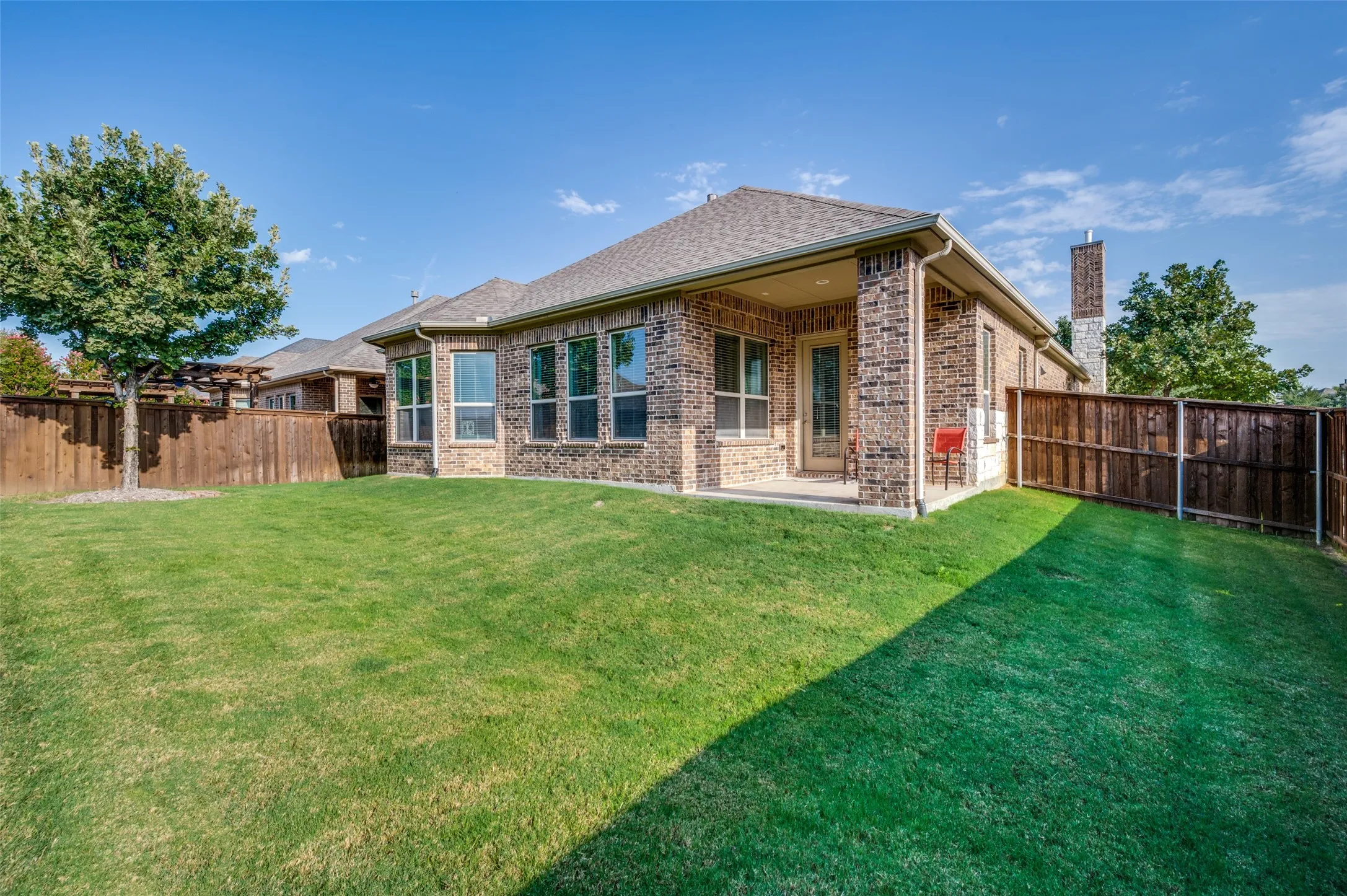Spacious, fully fenced backyard featuring a large grassy area and covered patio—perfect for relaxing, entertaining, pets, or outdoor play.