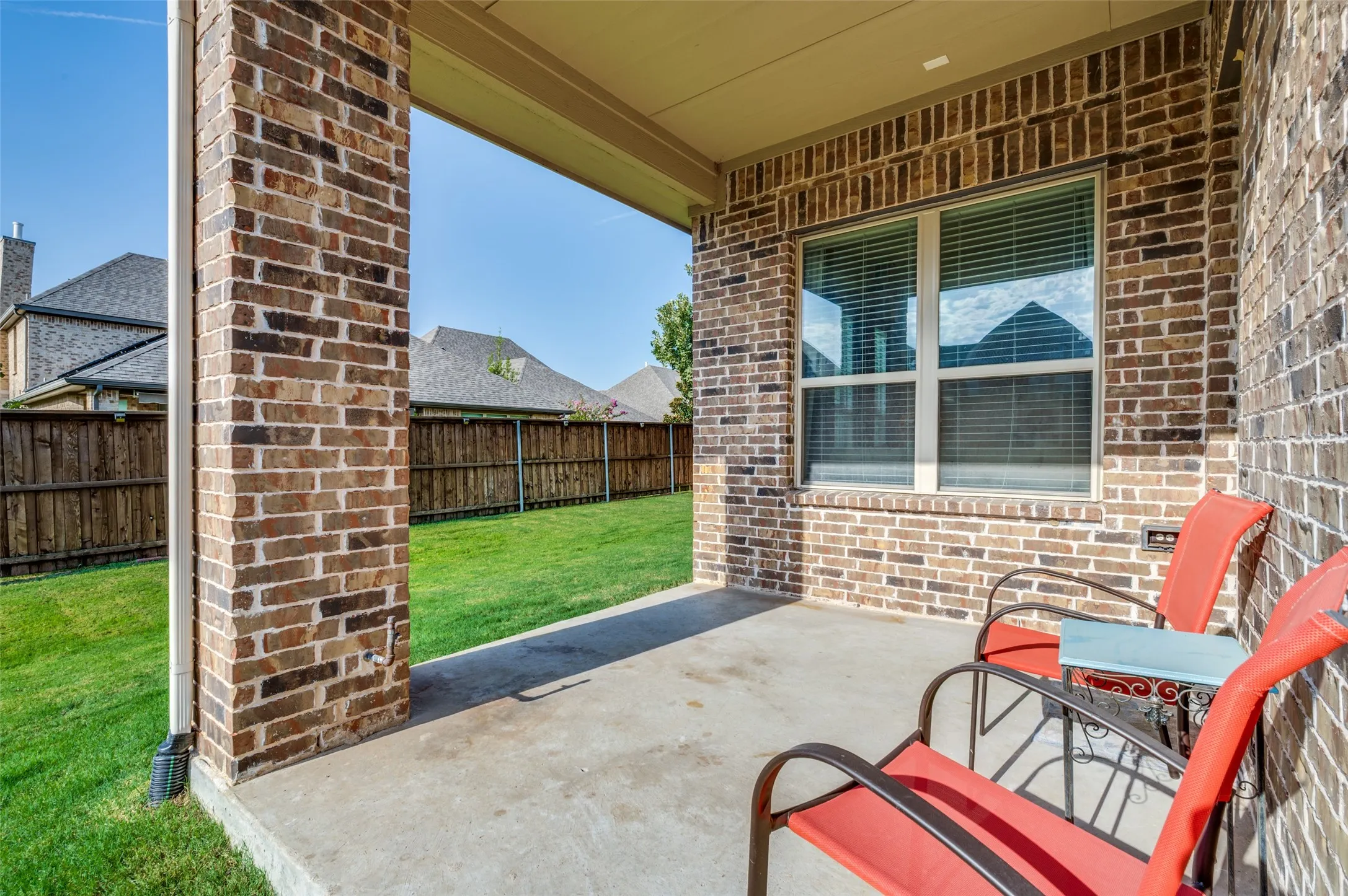 Covered backyard patio offering a great space for outdoor seating and entertaining, overlooking a spacious, fully fenced grassy yard.