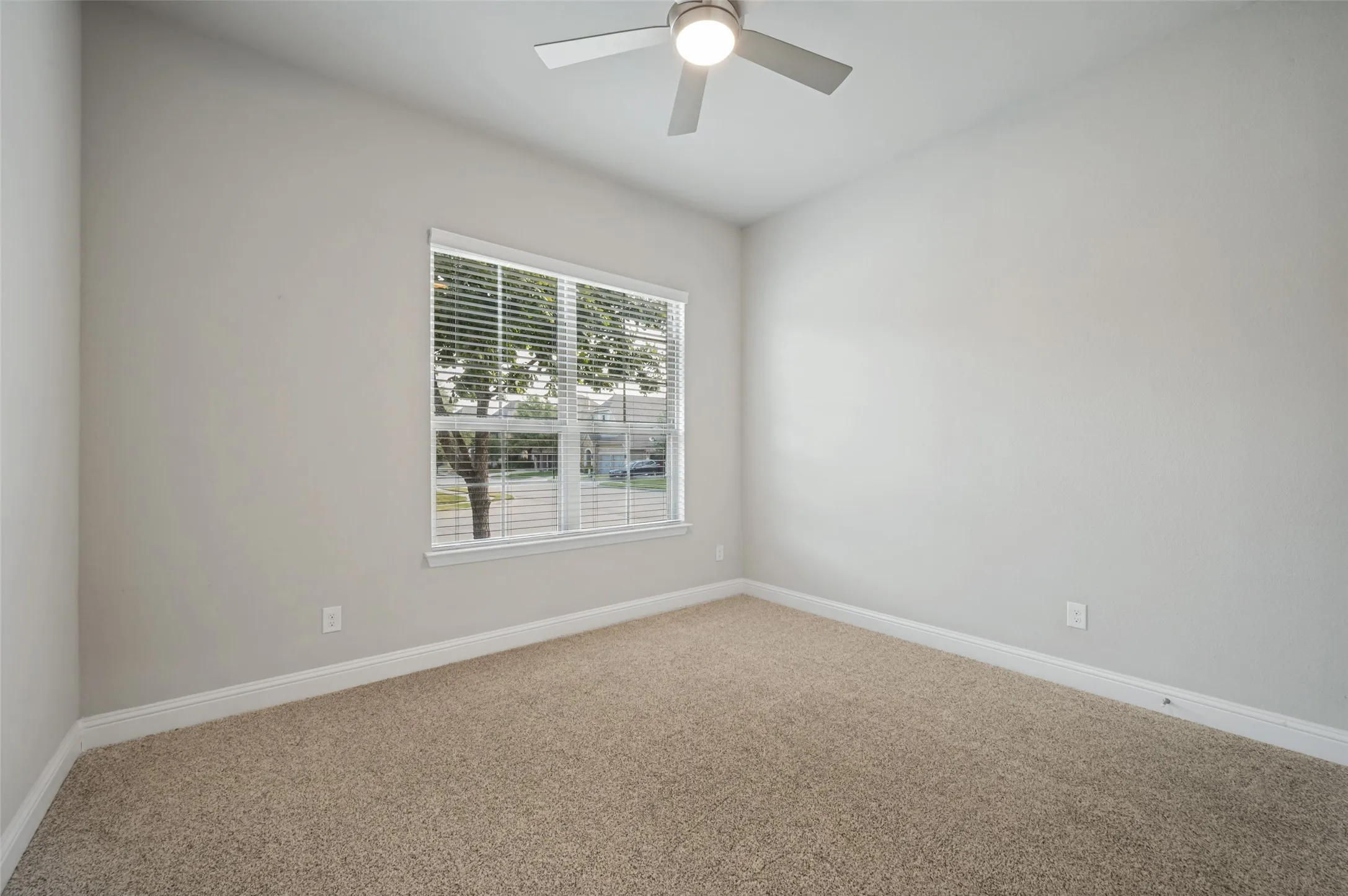 Spacious secondary bedroom featuring neutral finishes, plush carpeting, a ceiling fan, and a large window providing plenty of natural light.