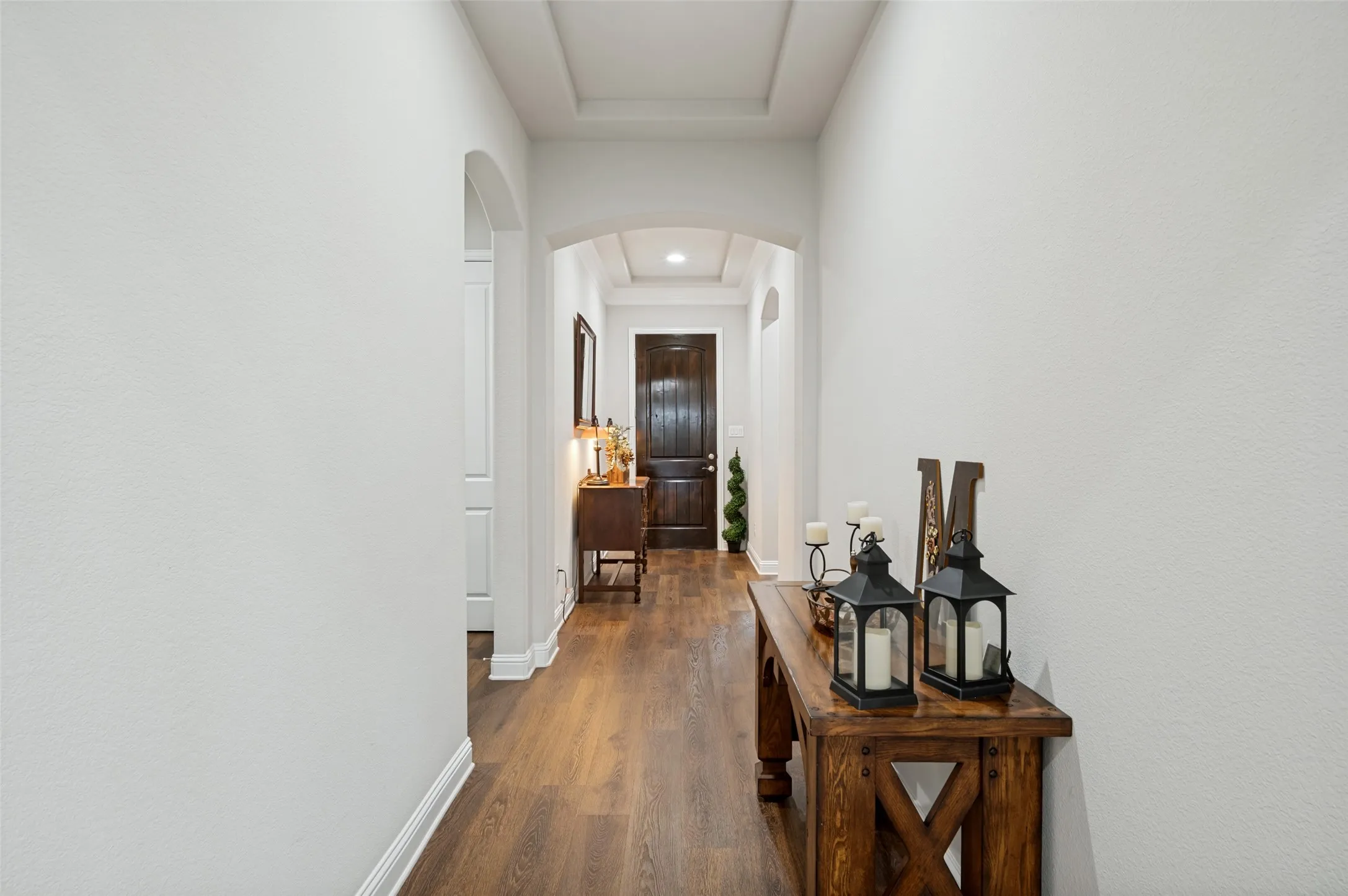 Inviting entryway featuring beautiful wood flooring, arched openings, tray ceiling details, and a warm, welcoming flow into the home.