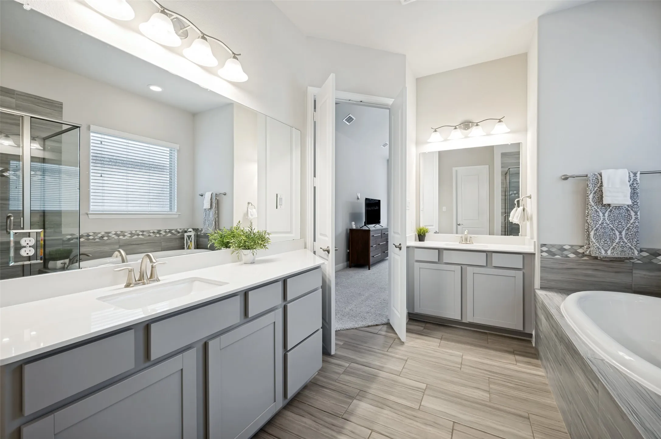 Spacious primary bath featuring separate vanities, generous counter and storage space, a soaking tub, glass-enclosed shower, and beautiful tile flooring for a relaxing retreat.