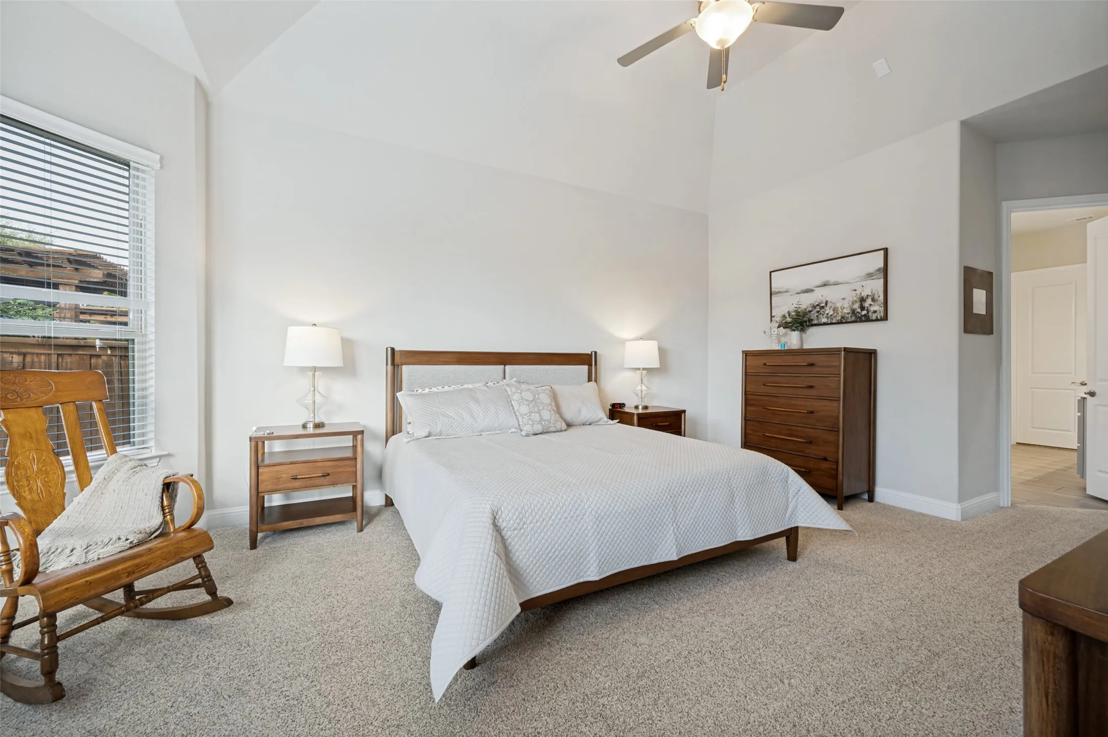 Spacious primary suite featuring a vaulted ceiling, plush carpeting, ceiling fan, and abundant natural light, with convenient access to the ensuite bath.