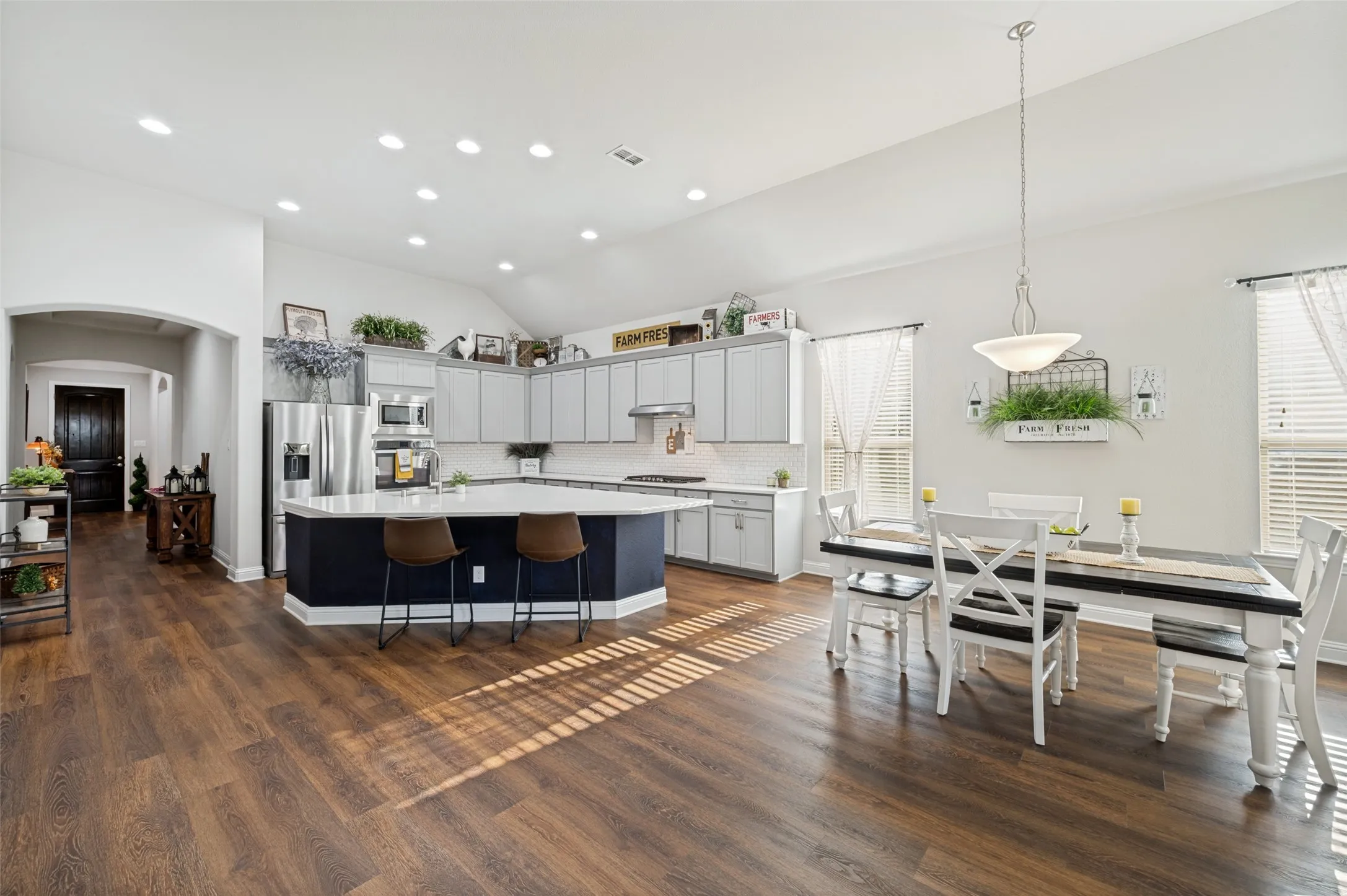 Spacious kitchen and dining area featuring vaulted ceilings, beautiful wood flooring, abundant cabinetry, a large center island with seating, stainless steel appliances, and plenty of natural light.