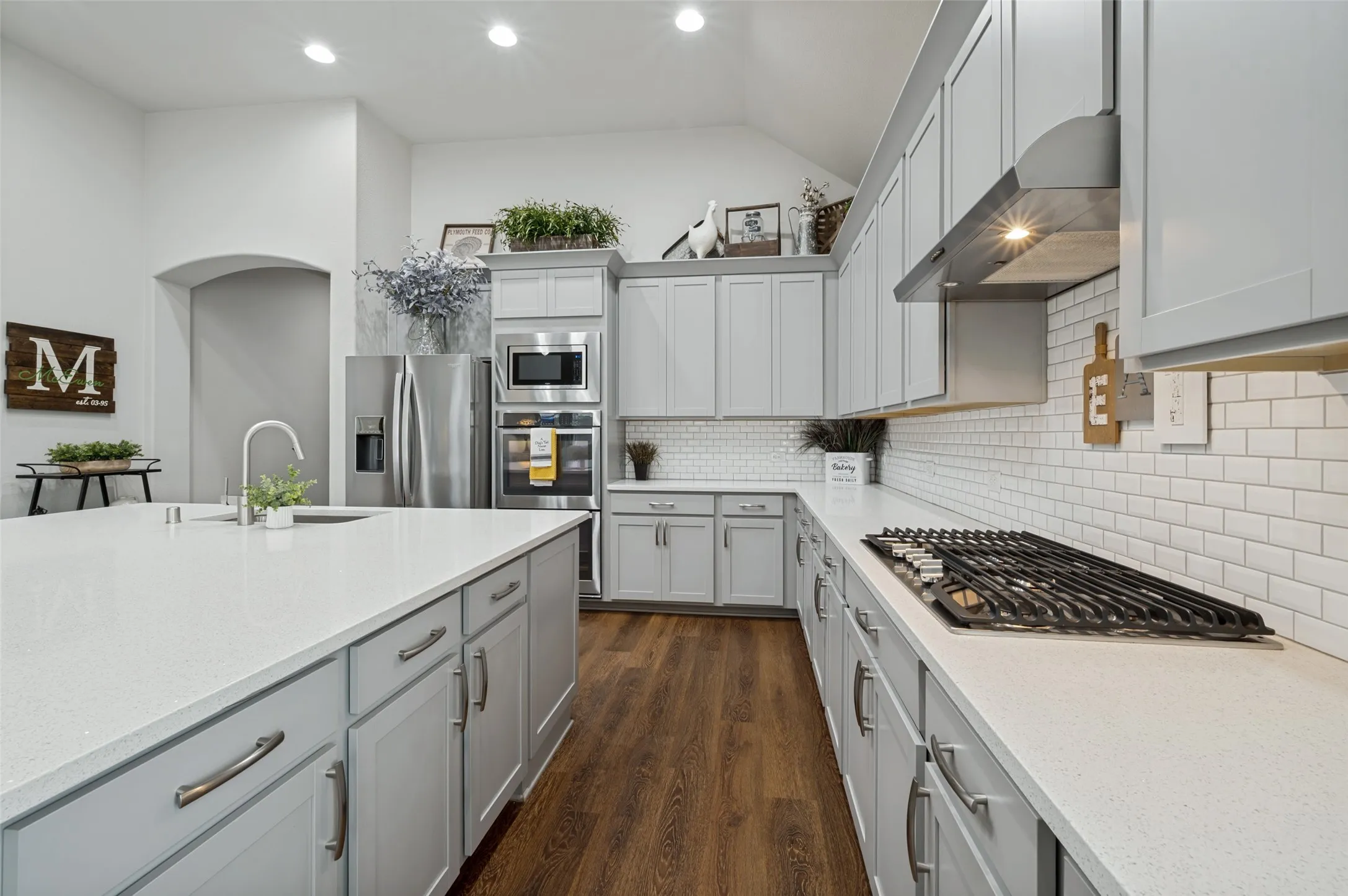 Well-appointed kitchen featuring a gas cooktop with stainless steel vent hood, quartz countertops, subway tile backsplash, abundant cabinetry, and stainless steel appliances.