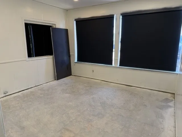 Recessed lighting illuminates a room featuring a concrete floor, wainscoting, and windows with roller shades