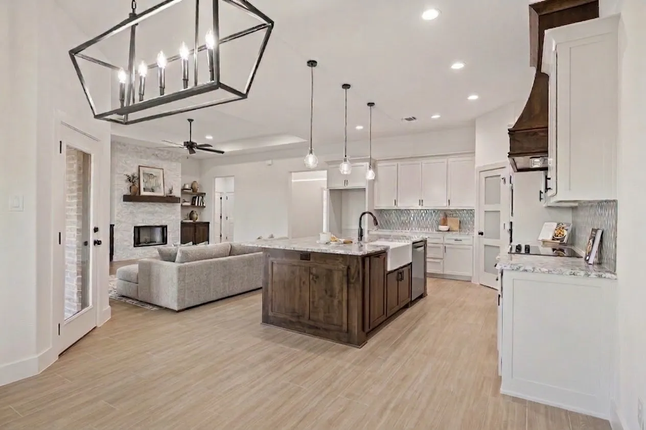 Wood-finish flooring throughout, kitchen island with built-in cabinetry, white shaker cabinetry, mosaic tile backsplash, and a fireplace with a stone surround