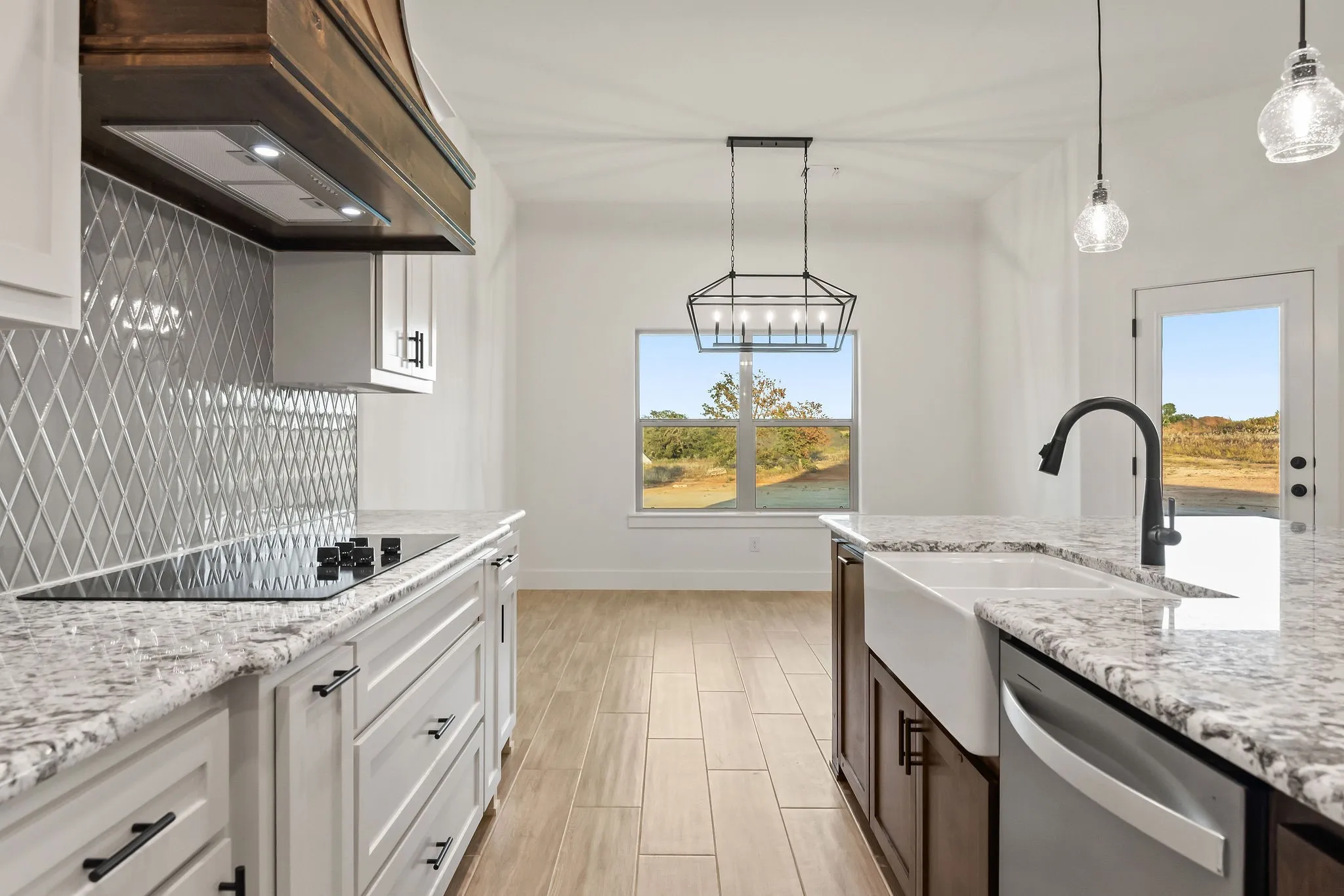Galley kitchen featuring white cabinetry, quartz countertops, stainless steel appliances including a farmhouse sink, geometric tile backsplash, pendant lighting, and wood-finish flooring throughout