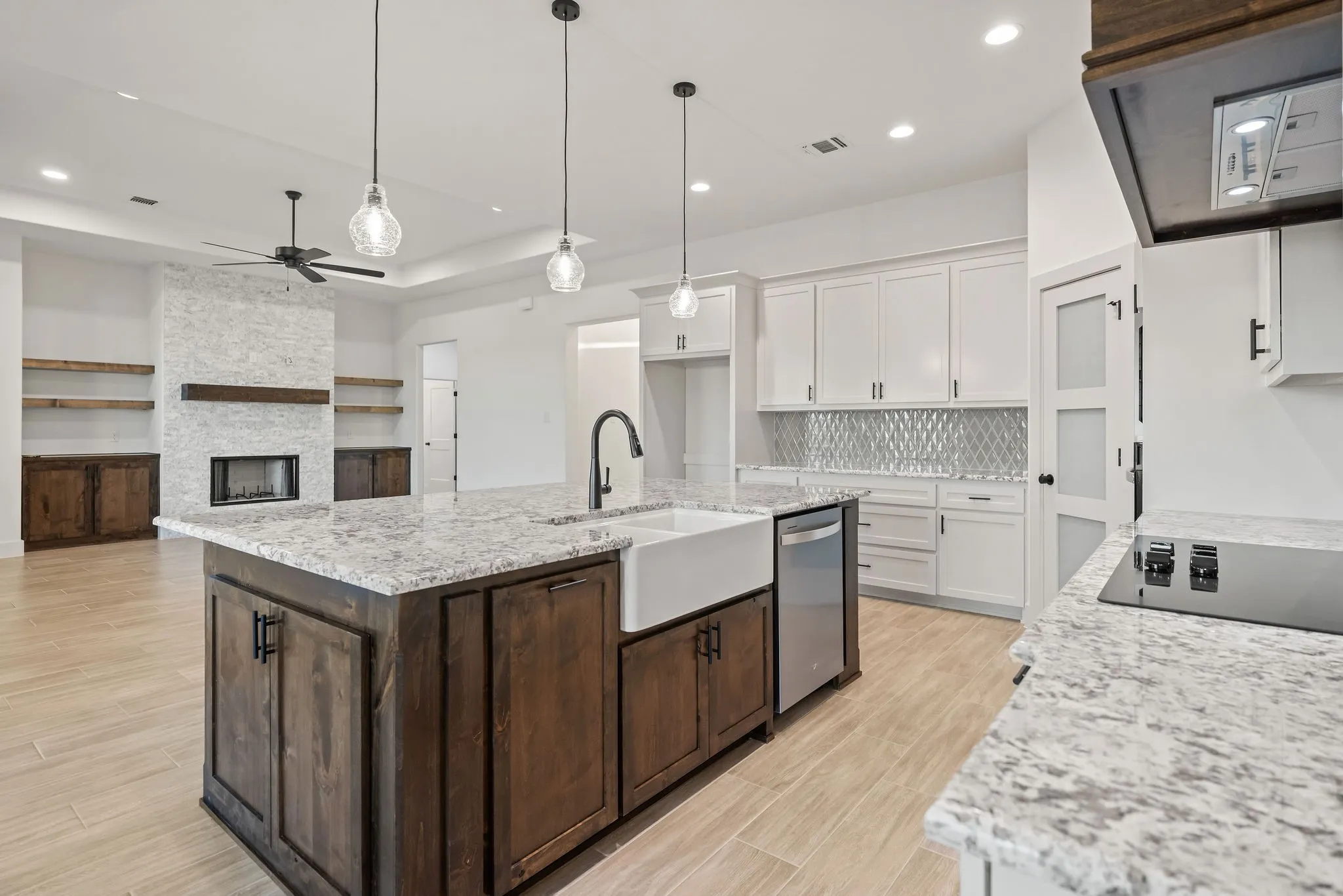Open-concept living space featuring a central kitchen island with a farmhouse sink, stainless steel dishwasher, and pendant lighting