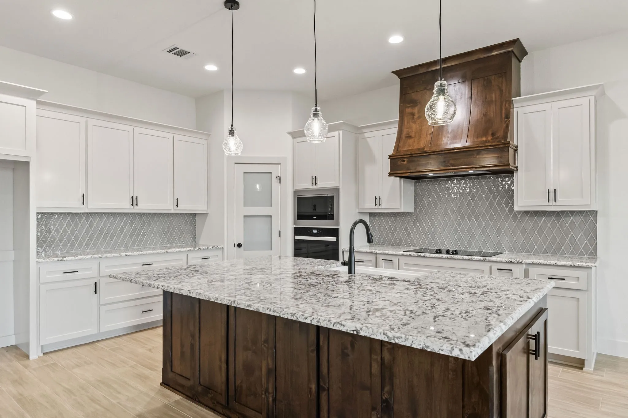 Chef's kitchen featuring white cabinetry, quartz countertops, stainless steel double wall ovens, a dark wood island with stone countertop surface, pendant lighting, geometric tile backsplash, and wood-finish flooring throughout