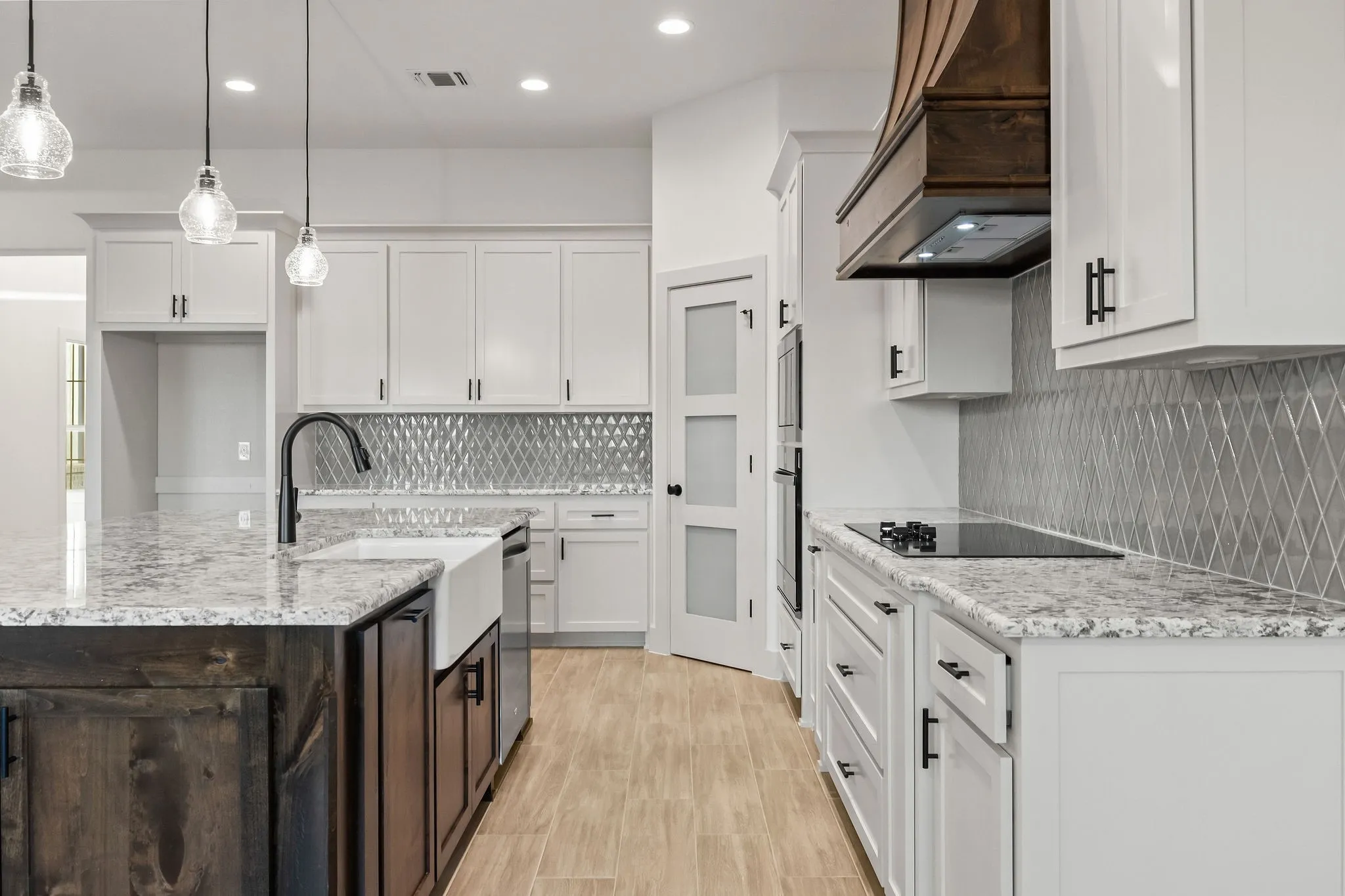 Chef's kitchen featuring white cabinetry with brushed nickel hardware, granite countertops, stainless steel appliances including a gas range and under-cabinet hood, a large center island with dark wood base and seating, geometric tile backsplash, pendant lighting, and wood-finish flooring throughout