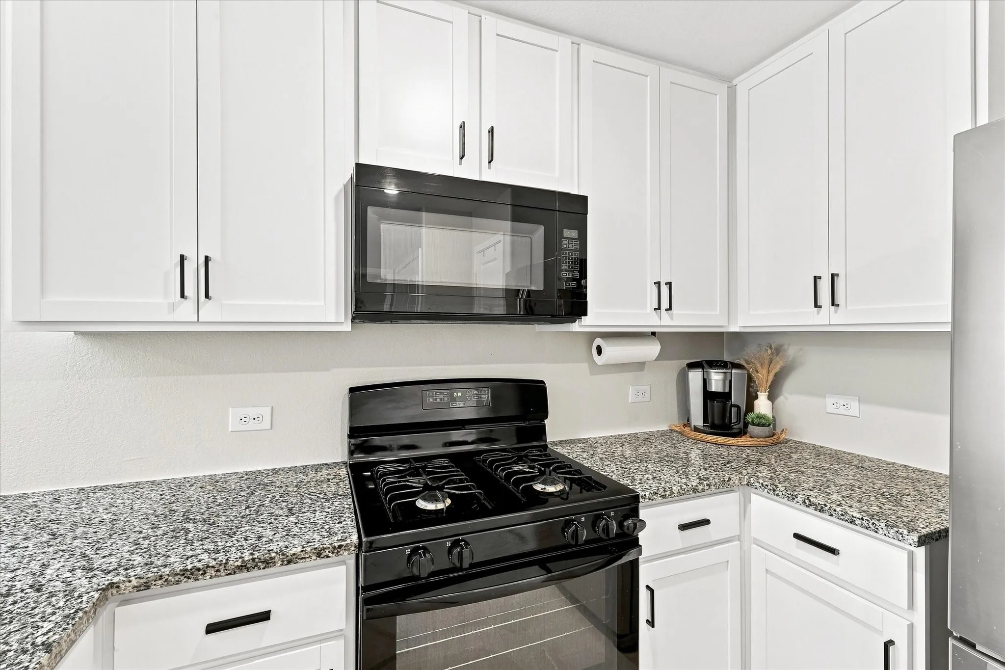 White cabinetry with black hardware, complementing black appliances, and speckled countertops