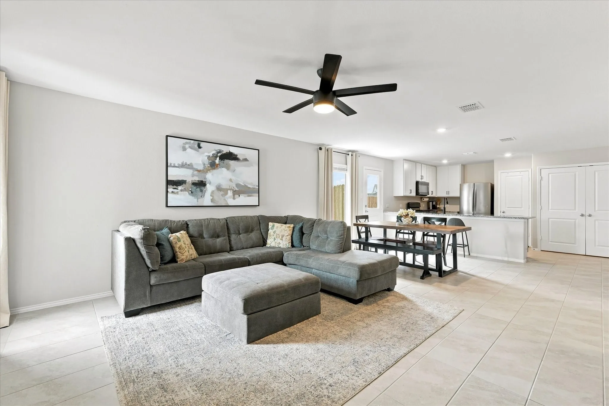 Open-concept living area with light tile flooring, a dark-finish ceiling fan, and recessed lighting