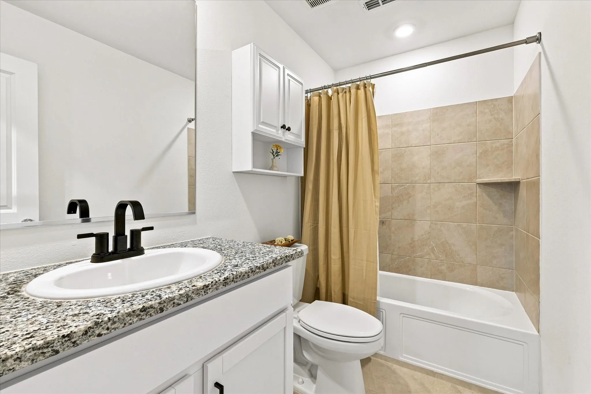 Granite-finish vanity countertop with an undermount sink and matte black faucet, white cabinetry, and tiled shower surround with an integrated niche