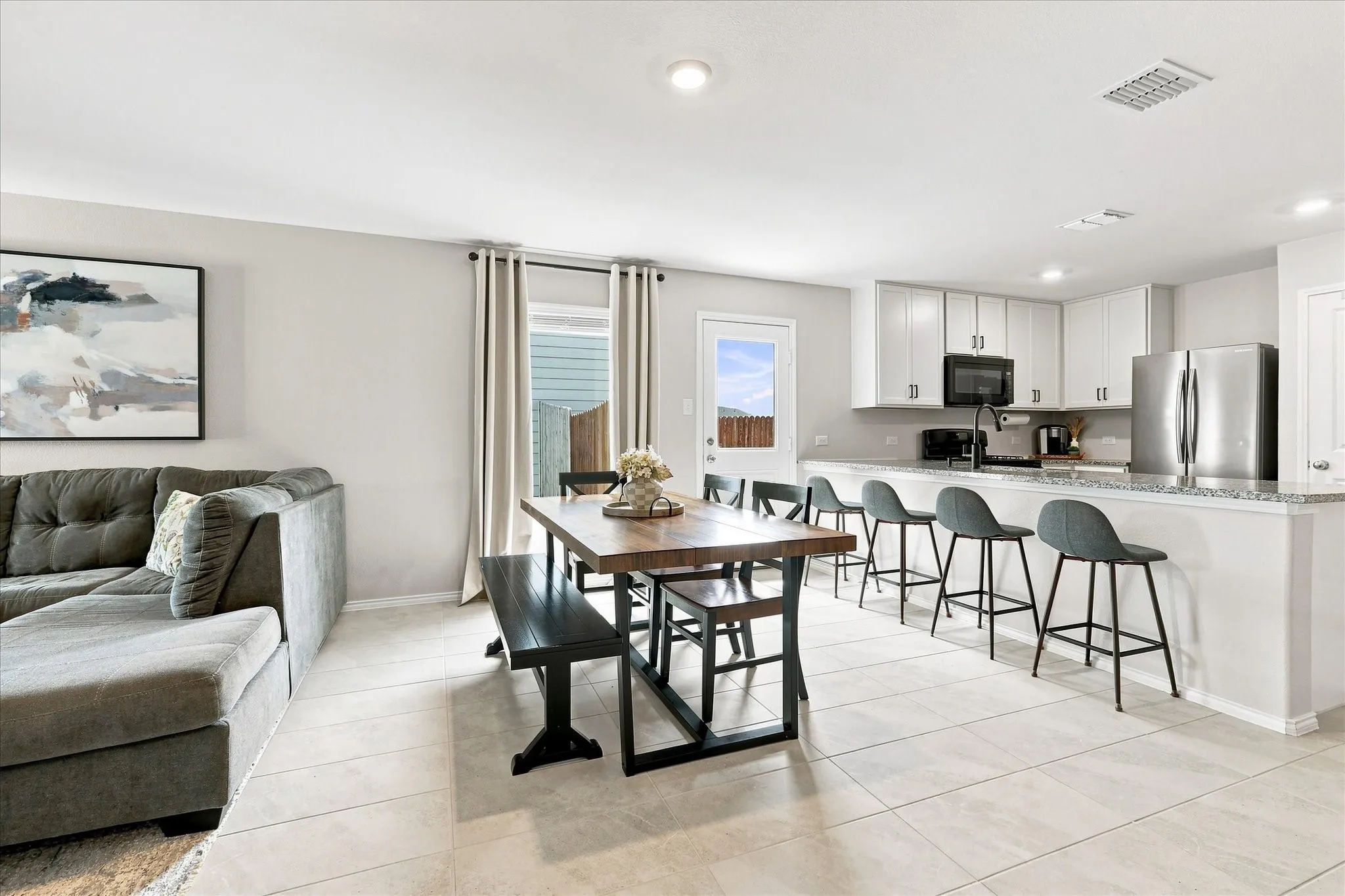 Open-concept living area featuring tile flooring, white kitchen cabinetry, stainless steel appliances, and a kitchen island with seating