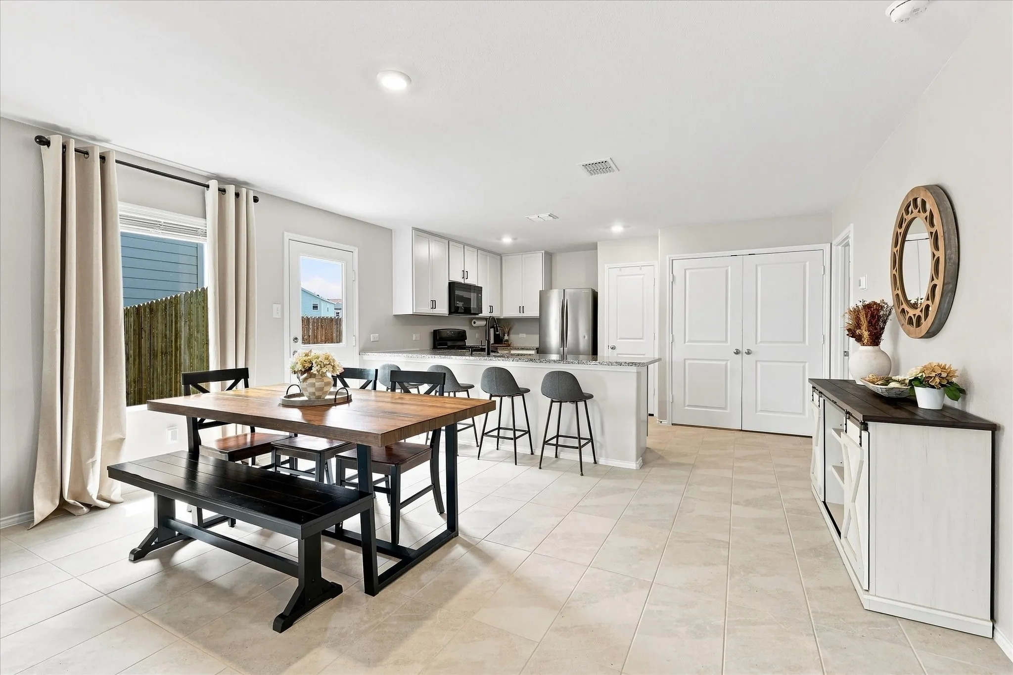 Open-concept design featuring tile flooring, white shaker cabinetry, stainless steel appliances, and a kitchen island with seating