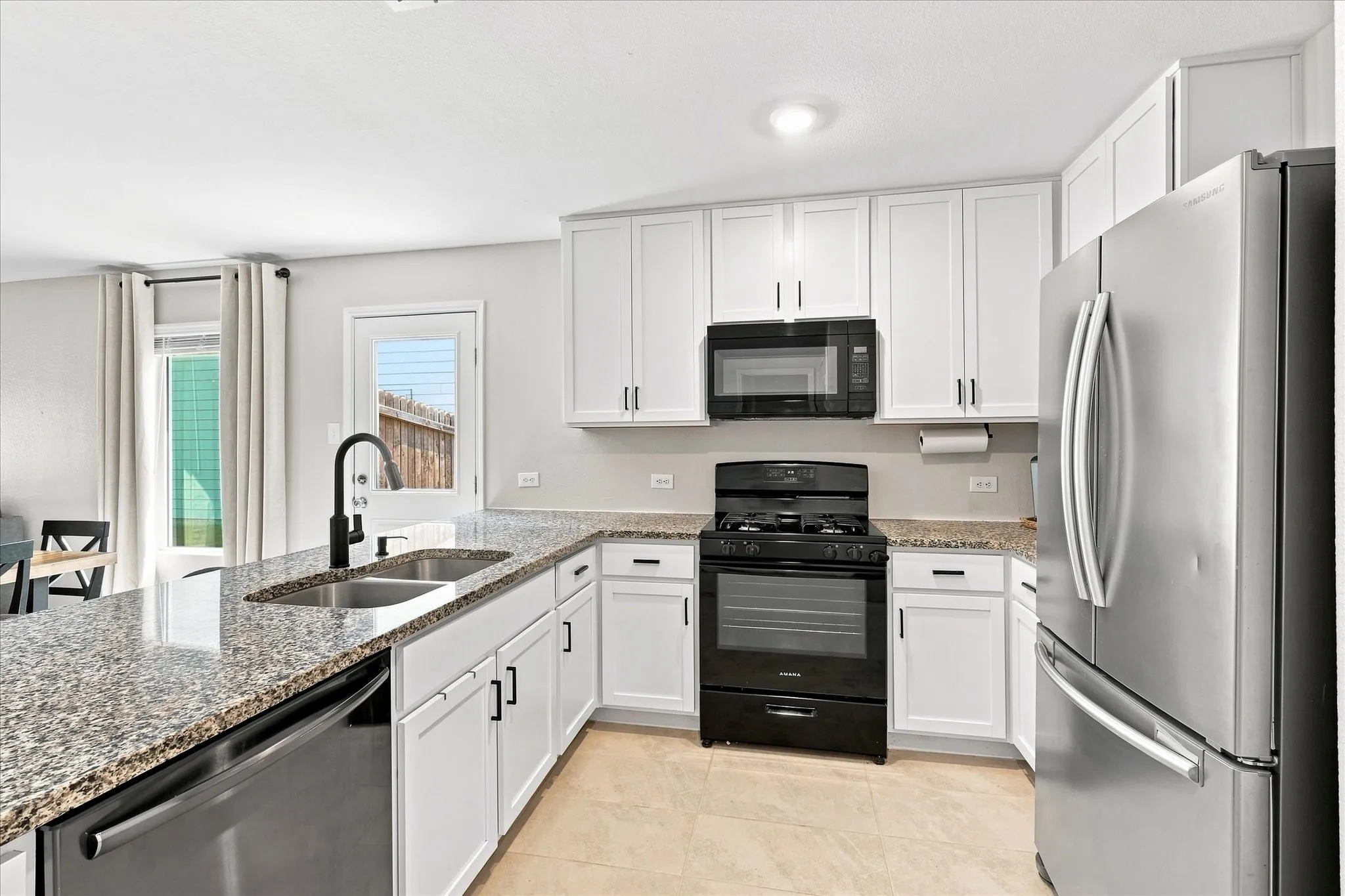 Modern kitchen featuring white cabinetry, granite-finish countertops, stainless steel appliances, and a double basin sink with a matte black faucet