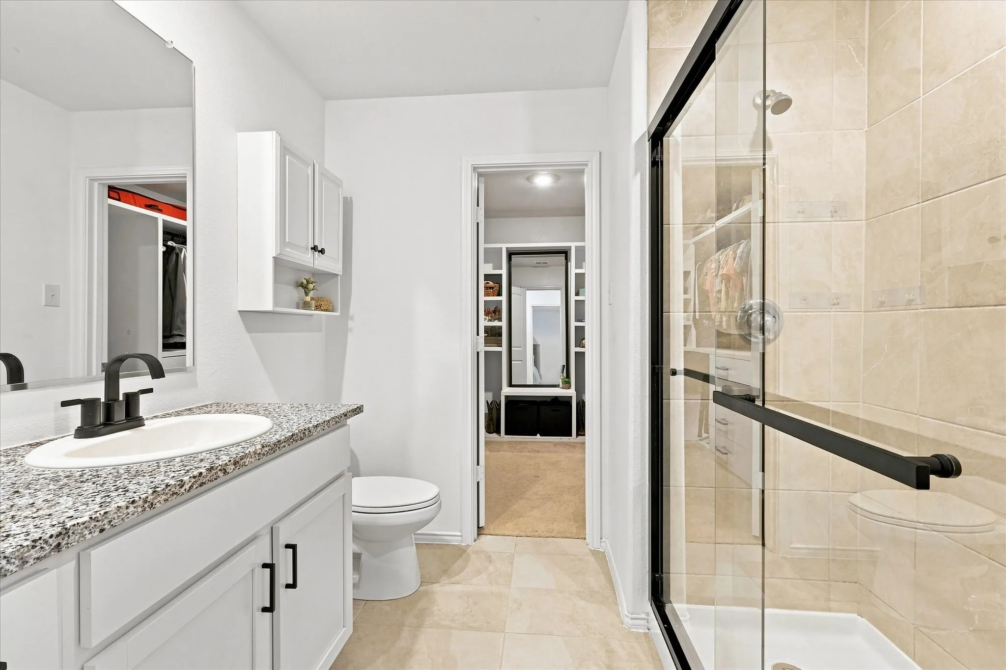 Vanity with a speckled countertop and undermount sink, white cabinetry with dark hardware, and a glass-enclosed shower with tiled walls
