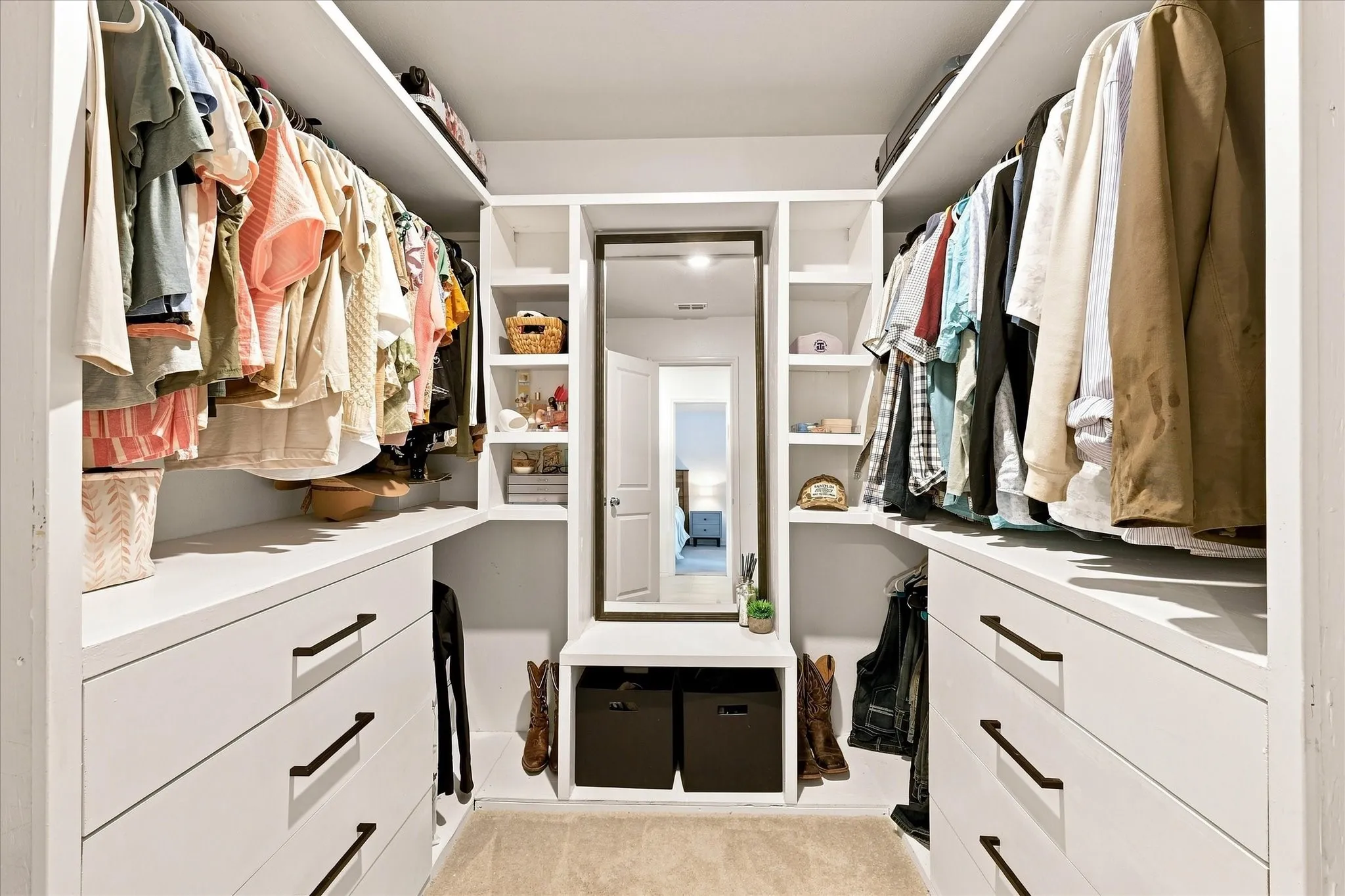 Built-in closet system featuring multiple hanging rods, integrated shelving, ample drawer storage with black hardware, and a framed mirror